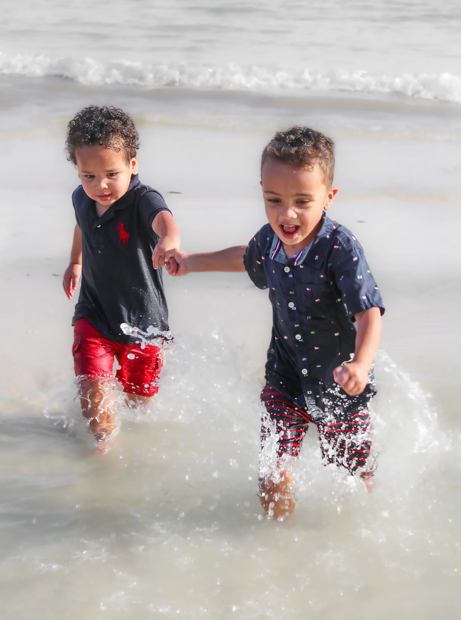 Dos niños hermanos corriendo y riendo en la orilla del mar durante una sesión de fotos familiar en el Caribe.