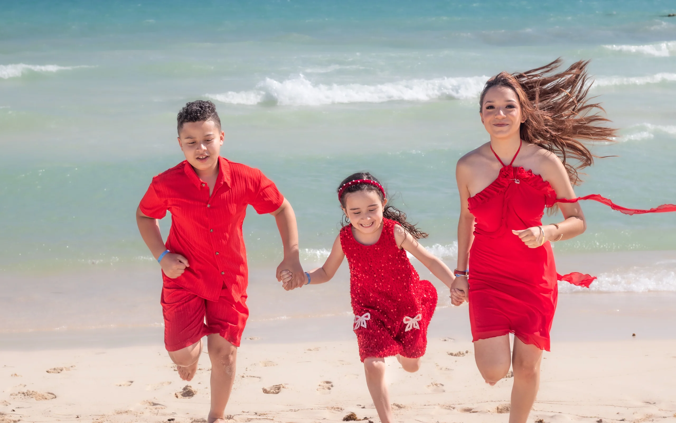 niños posando juntos y sonrientes frente al mar azul en una playa de arena blanca.