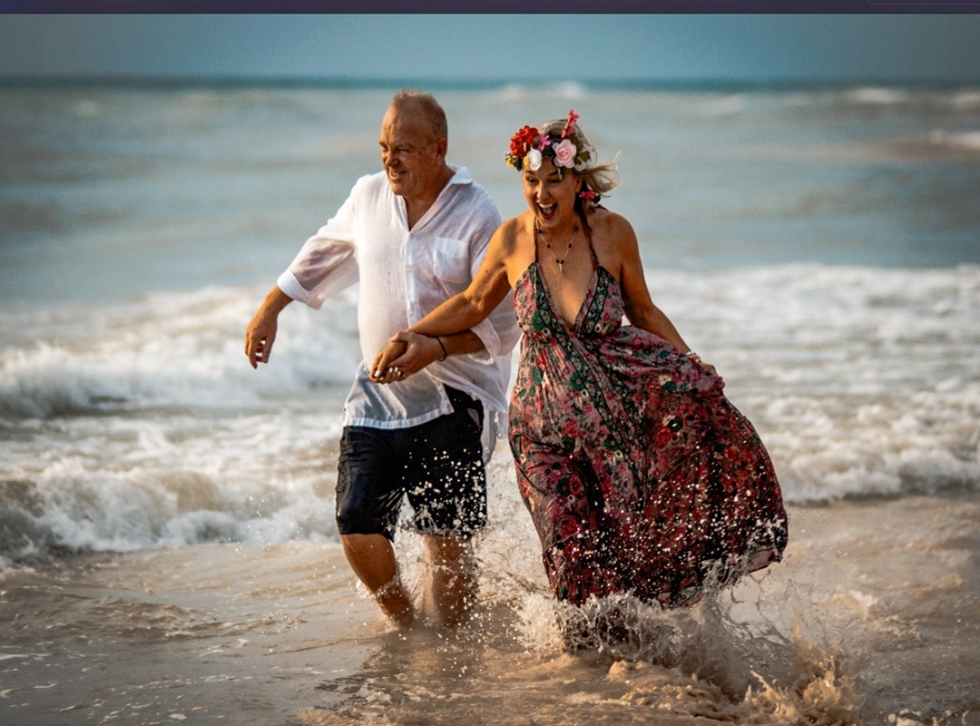 Couple running and laughing in the ocean during a romantic sunset beach photoshoot.