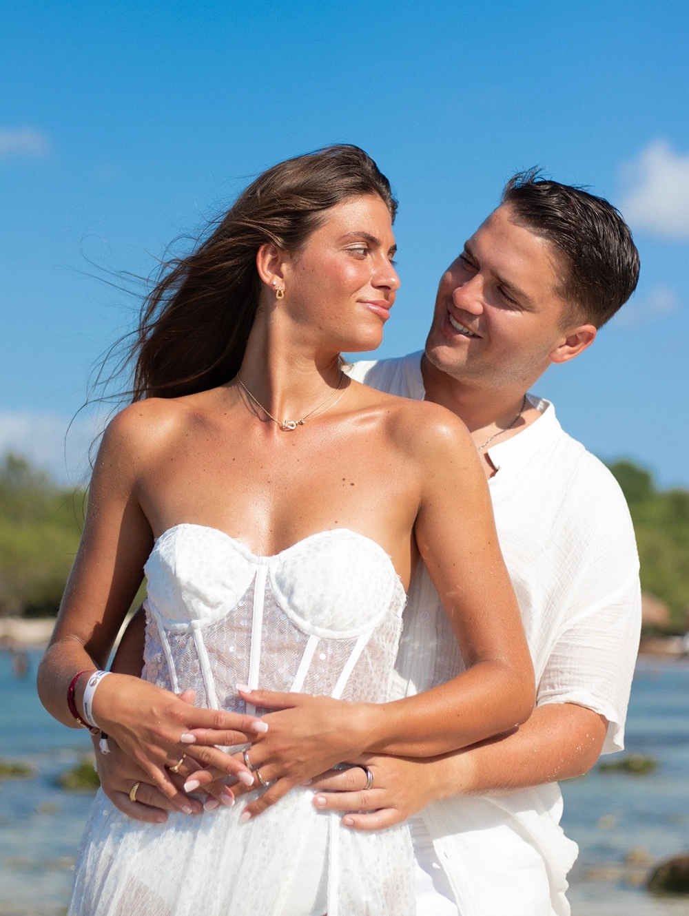 Retrato de novios en la Riviera Maya: pareja feliz en la playa, ella con vestido de novia blanco con corsé de encaje.