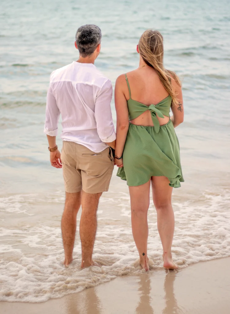 Pareja joven caminando de la mano por la orilla de una playa del Caribe mexicano, vistos desde atrás.