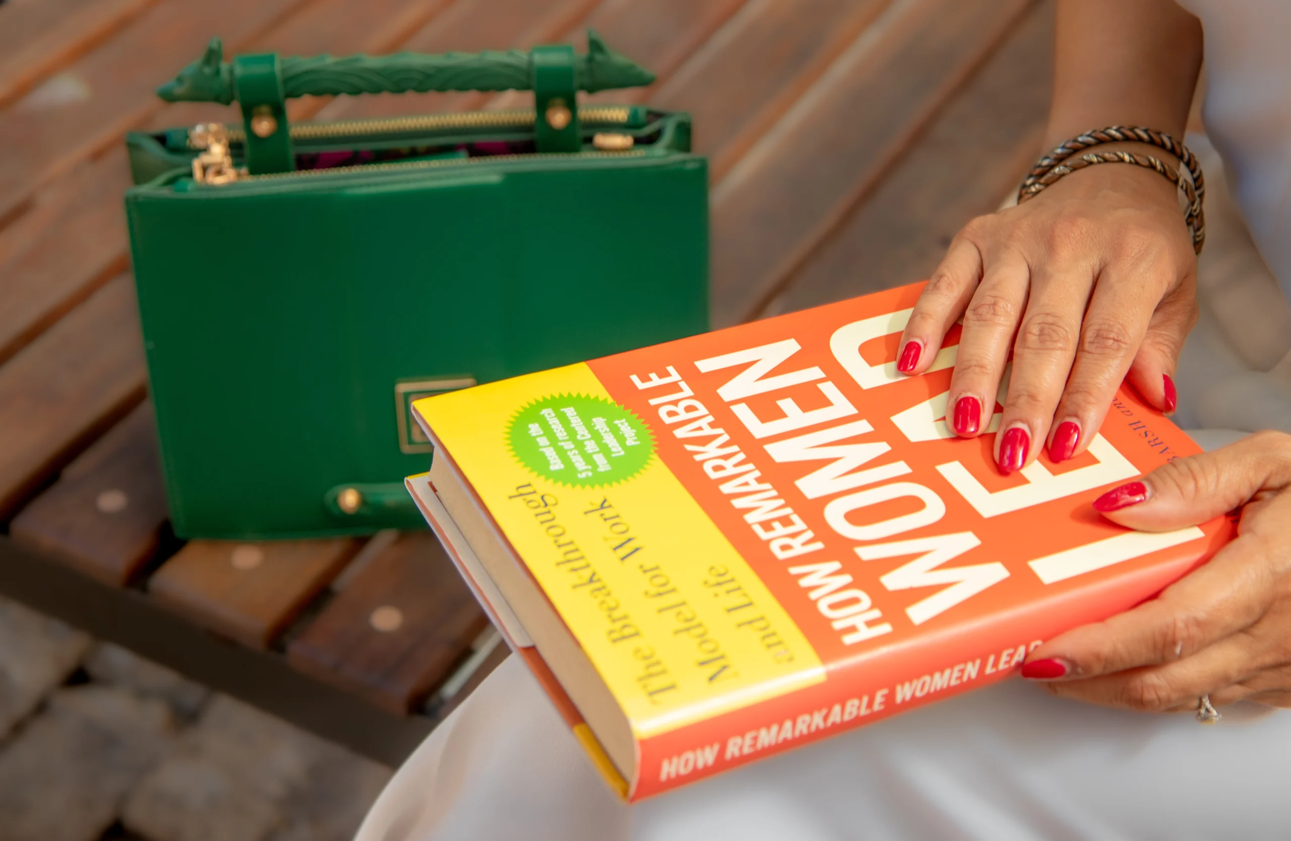 Manos femeninas con uñas rojas sosteniendo un libro y bolso verde - personal branding lifestyle